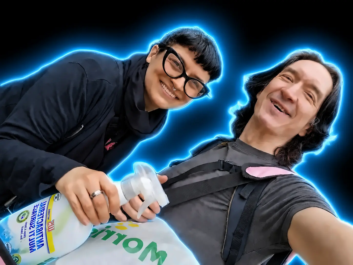 David and Kari smiling mid cleaning shift, spray bottle and shopping bag in hand, outlined in electric blue